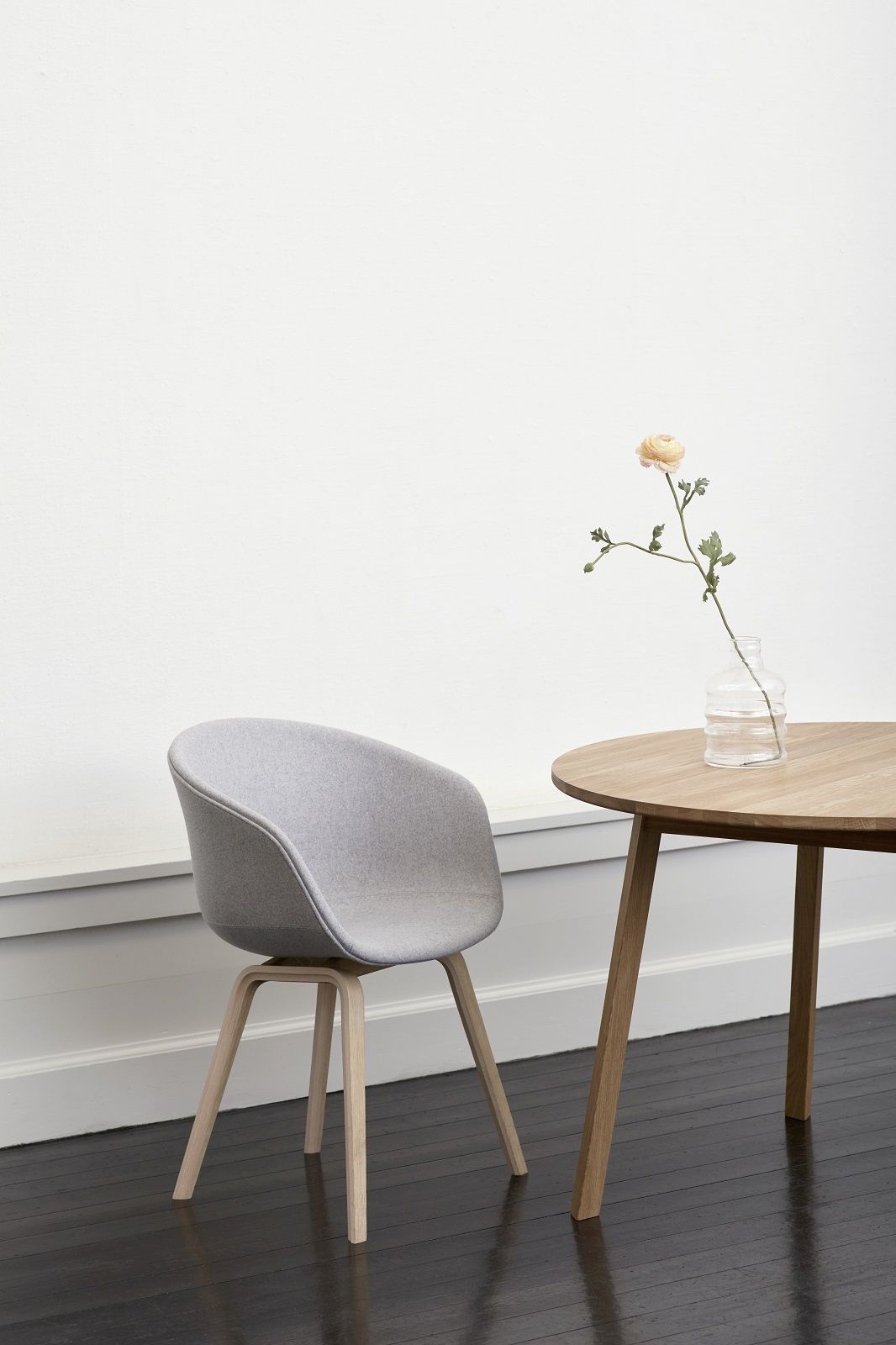 Hay Triangle Leg Table Esstisch mit Stuhl und Blume in Vase auf dunklem Holzboden.