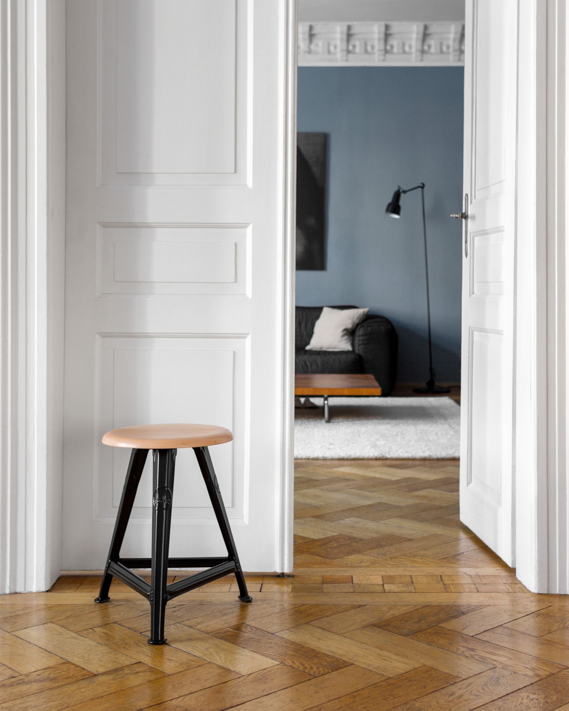 Hocker aus Holz und Metall vor offener Tür auf Parkettboden. Design Hocker kaufen.