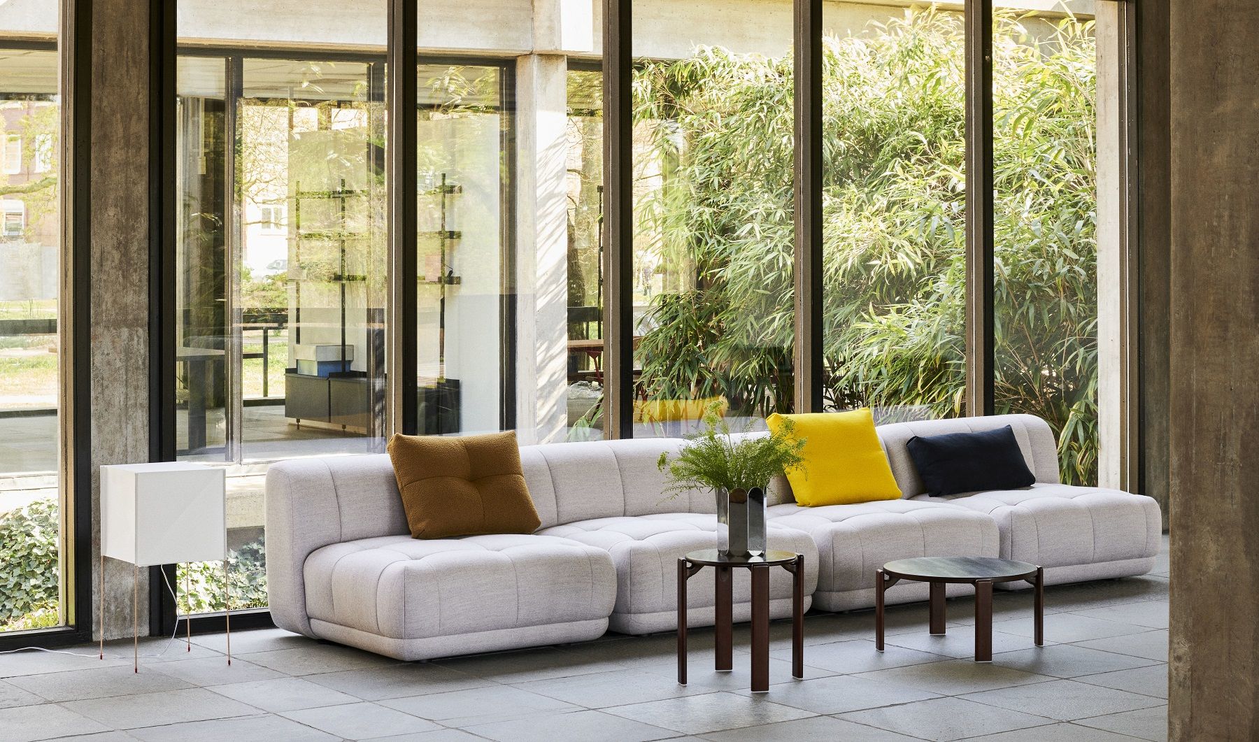 Helles Wohnzimmer mit modularem Sofa, Beistelltischen und Kissen, im Hintergrund Fenster mit Blick auf Bambus.