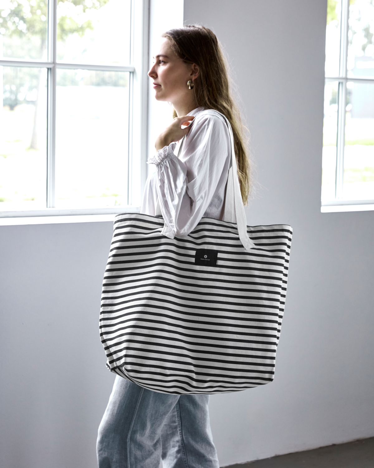 Frau mit gestreifter HDCanva Tasche von House Doctor in Schwarz und Off-White vor Fenster.