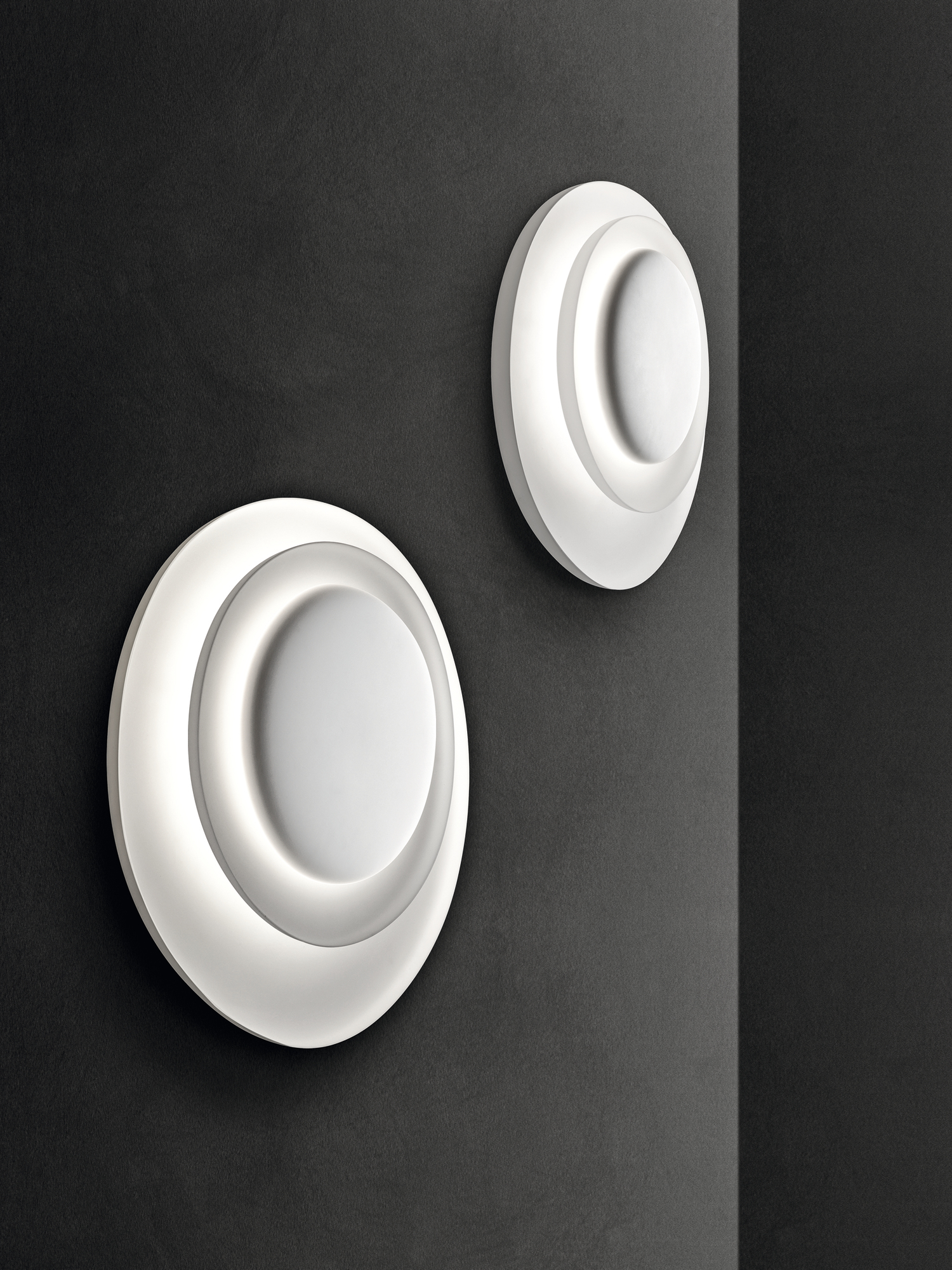 Zwei moderne, runde Bahia Wandleuchten von Foscarini in Weiß an einer dunklen Wand.