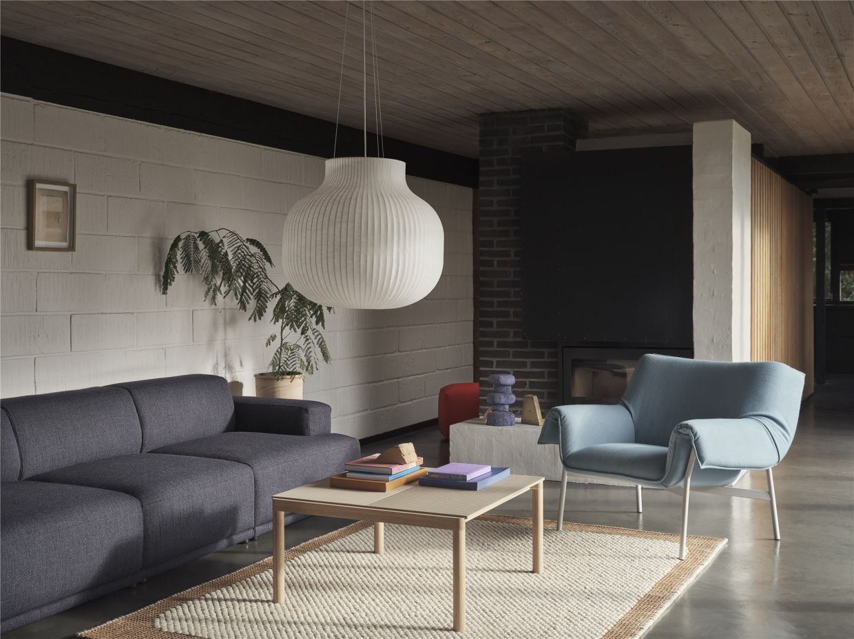 Wohnzimmer mit grauer Couch, blauem Sessel, Holztisch und großer, weißer Hängeleuchte für gemütliche Atmosphäre.