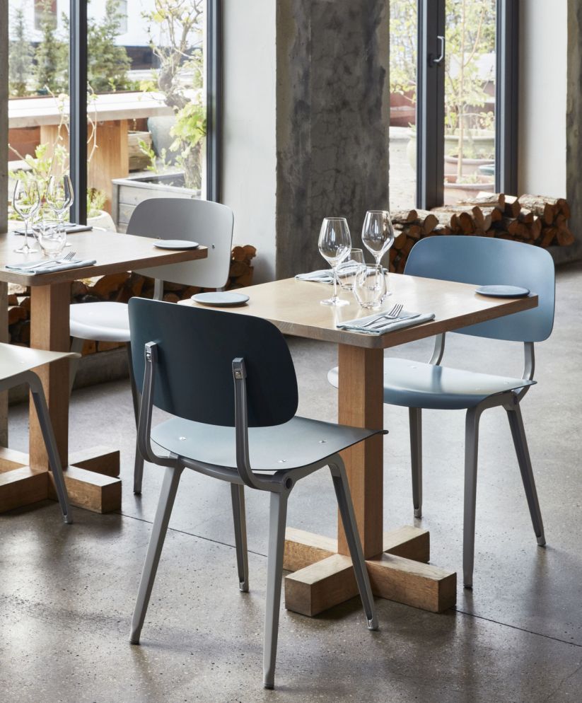Mehrere Hay Revolt Stühle in Blau und Grau an Holztischen in einem Restaurant.