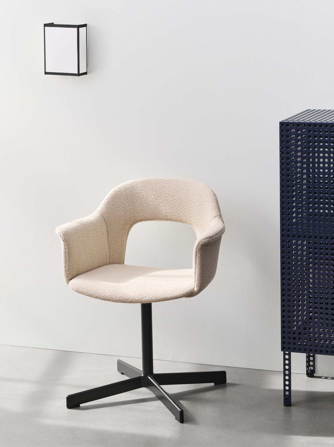 Beiger Hay Layout Armchair 234 Armlehnstuhl mit schwarzem Drehfuß vor weißer Wand und blauem Schrank.