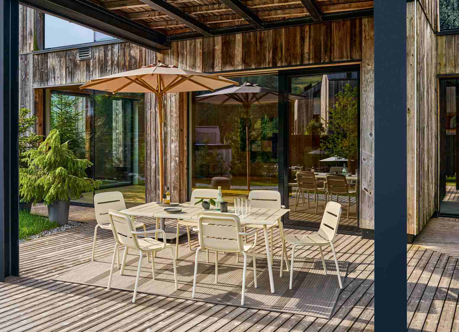 Vapio Sessel Outdoor Weishäupl: Gartenset mit Esstisch und Stühlen auf einer Holzterrasse mit Sonnenschirm.