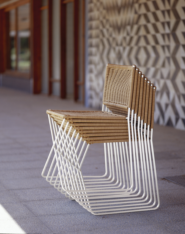 Gestapelte Ramón Rattanstühle von Santa & Cole mit weißem Metallgestell und Rattan-Sitzfläche.