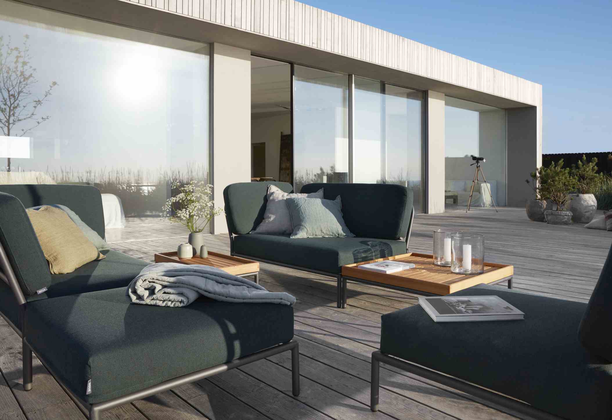 Houe Level Outdoor Sofa-Set auf einer Terrasse mit Holzboden und großem Fenster im Hintergrund.