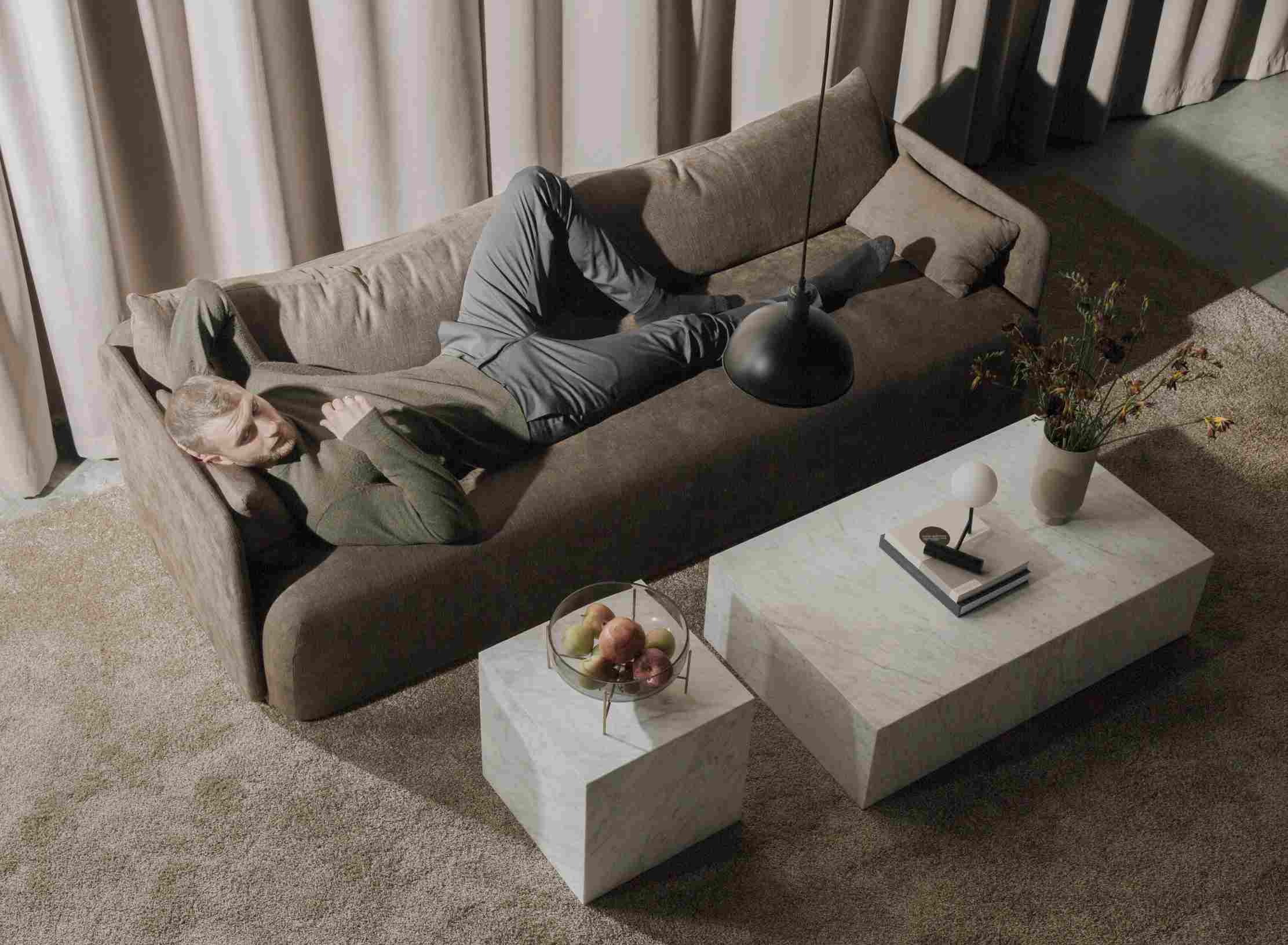 Mann entspannt auf Sofa neben Audo Copenhagen Plinth Tisch aus Marmor, minimalistisches Wohnzimmer Design.