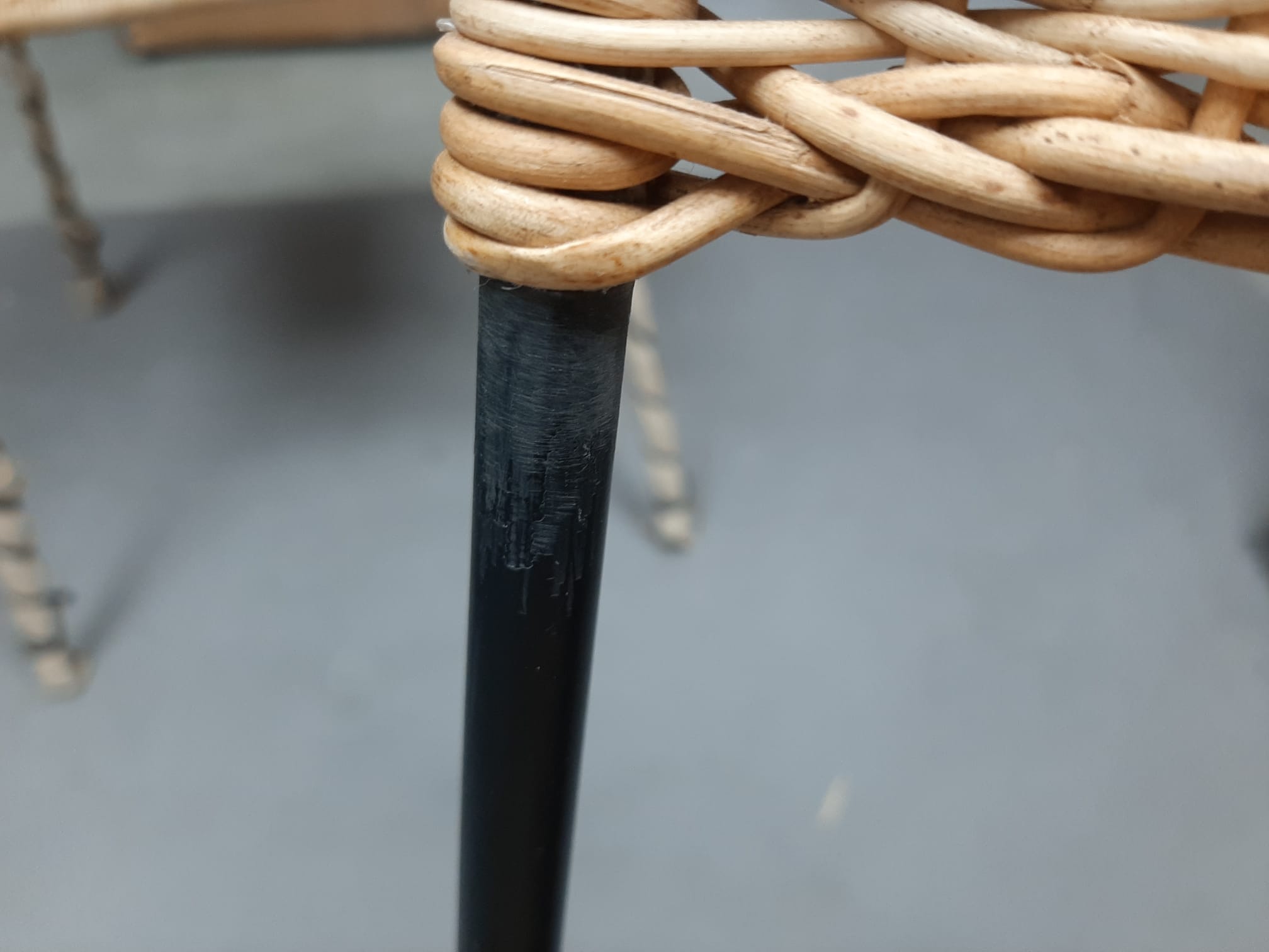 Detailaufnahme eines Richard Lampert Stuhls mit schwarzem Metallbein und geflochtener Sitzfläche aus Rattan.