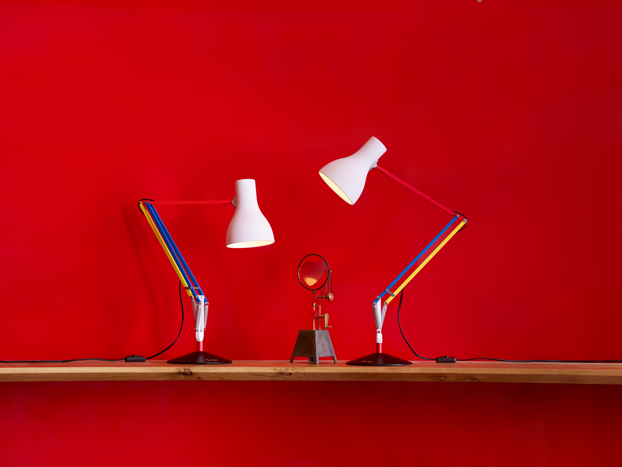 Zwei Anglepoise Type 75 Mini Paul Smith Edition Tischleuchten in Weiß und bunten Akzenten auf Holzregal.