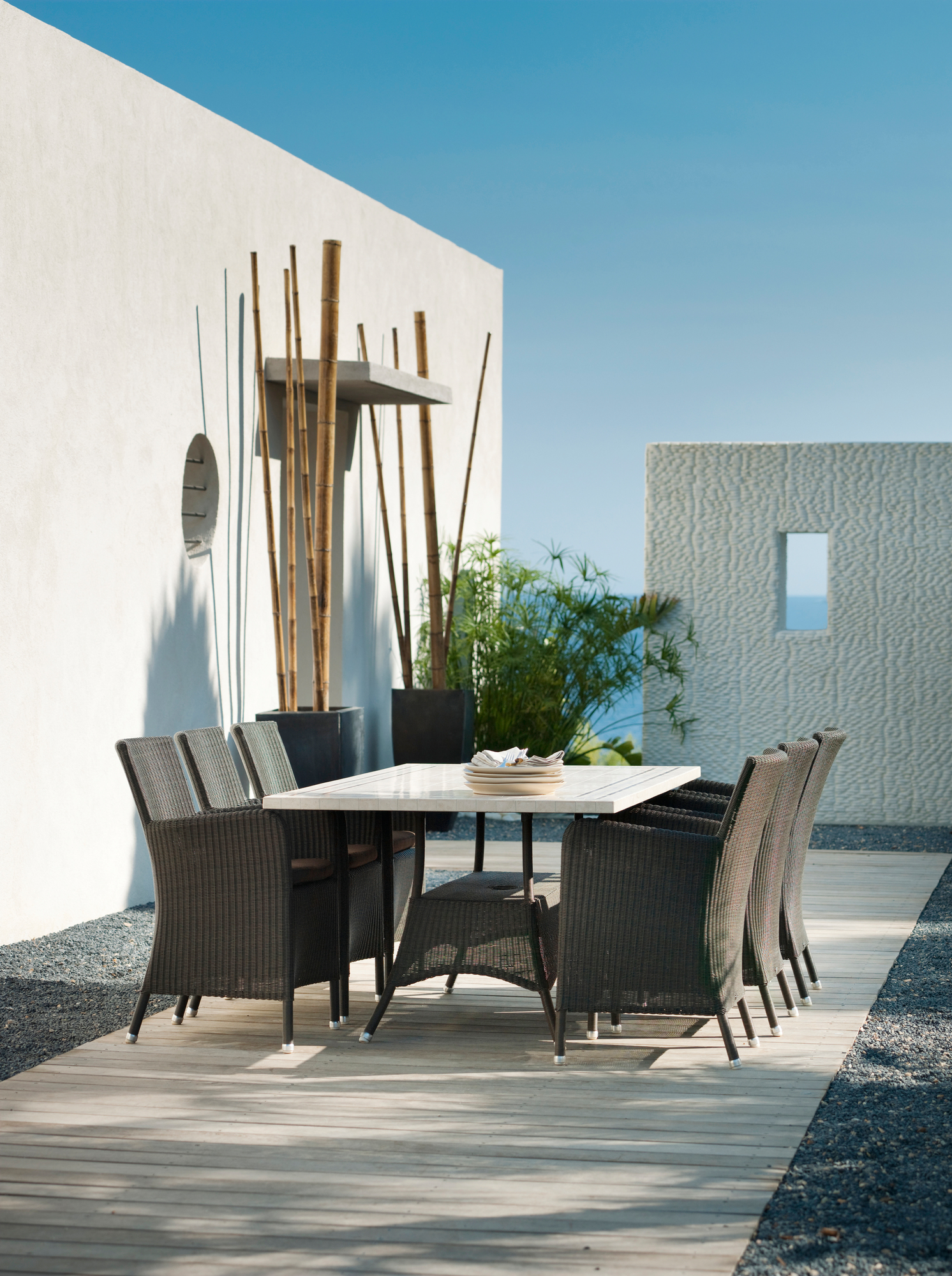 Cane-Line Hampsted Gartensessel und Esstisch aus Rattan auf einer Holzterrasse mit modernem Hintergrund.
