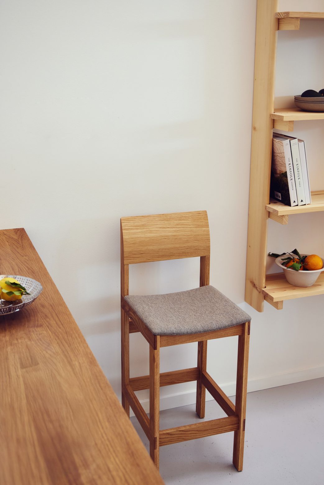 Sonder Barhocker 65 von Form & Refine aus Eichenholz mit grauem Polstersitz.