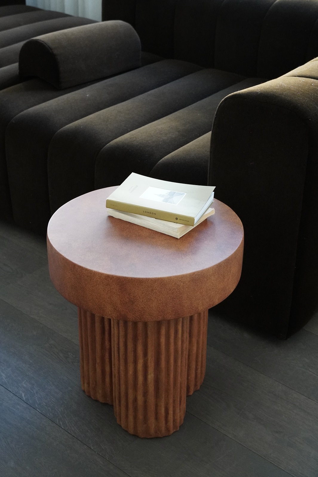 Nahaufnahme des Gear Tall Side Table von Norr11 in Terrakotta mit Büchern, neben einem dunklen Sofa.