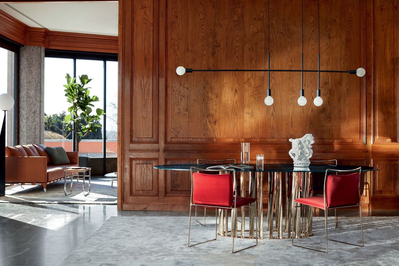 Esszimmer mit Cassina Boboli Tisch, Glasplatte und goldenem Gestell, rote Stühle.