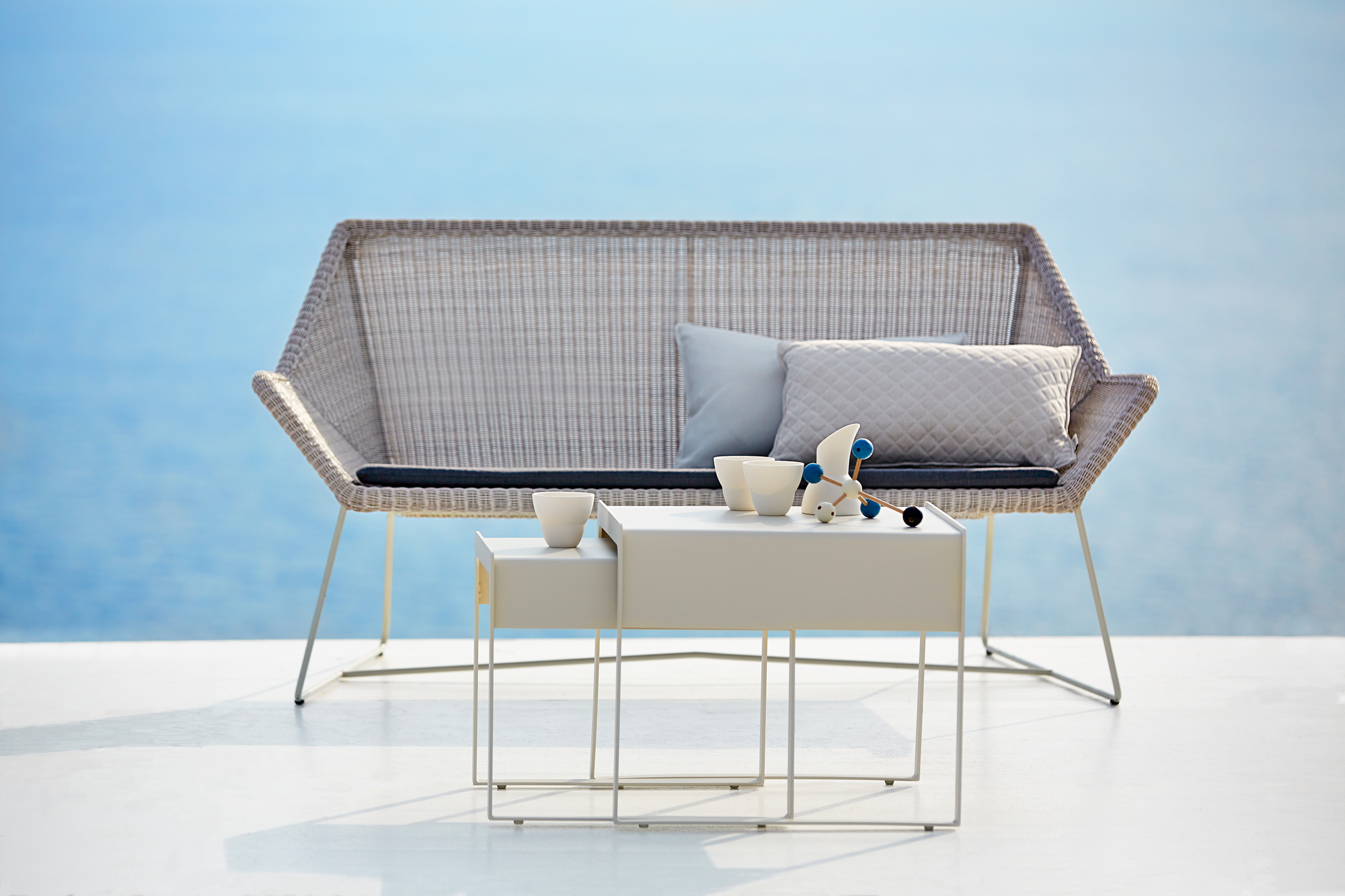 Breeze Loungesofa von Cane-Line: Graues Outdoor Sofa mit Kissen und Beistelltisch.