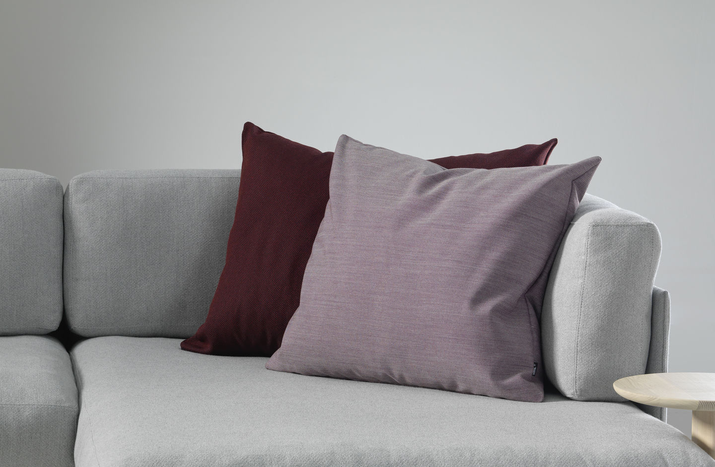 Vitra Kissen: Zwei Zierkissen in Lila und Weinrot auf einem grauen Sofa, Nahaufnahme.
