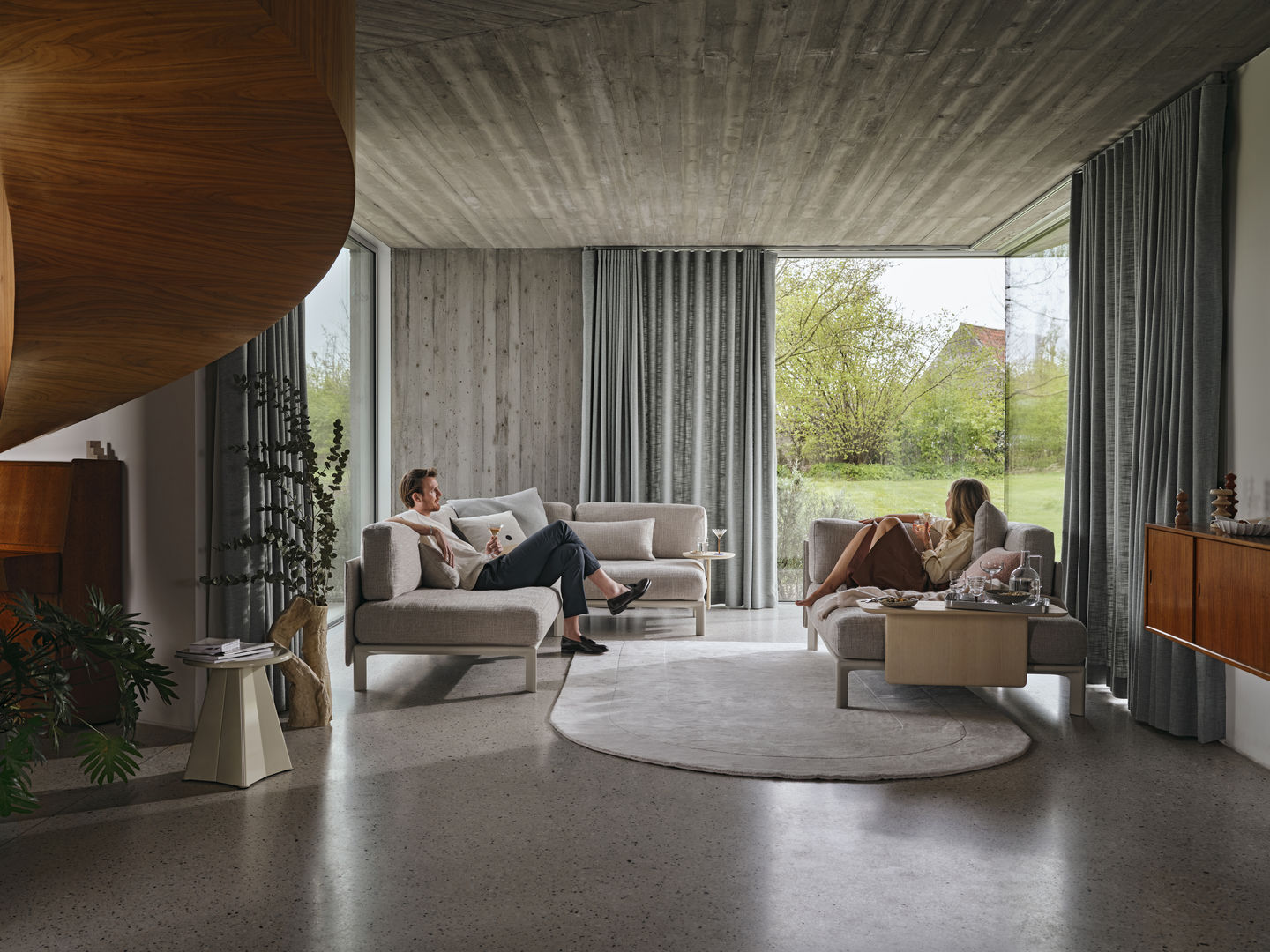 Helle Wohnzimmer-Szene mit zwei Personen auf grauen Vitra Anagram Sofas, modernes Möbeldesign.
