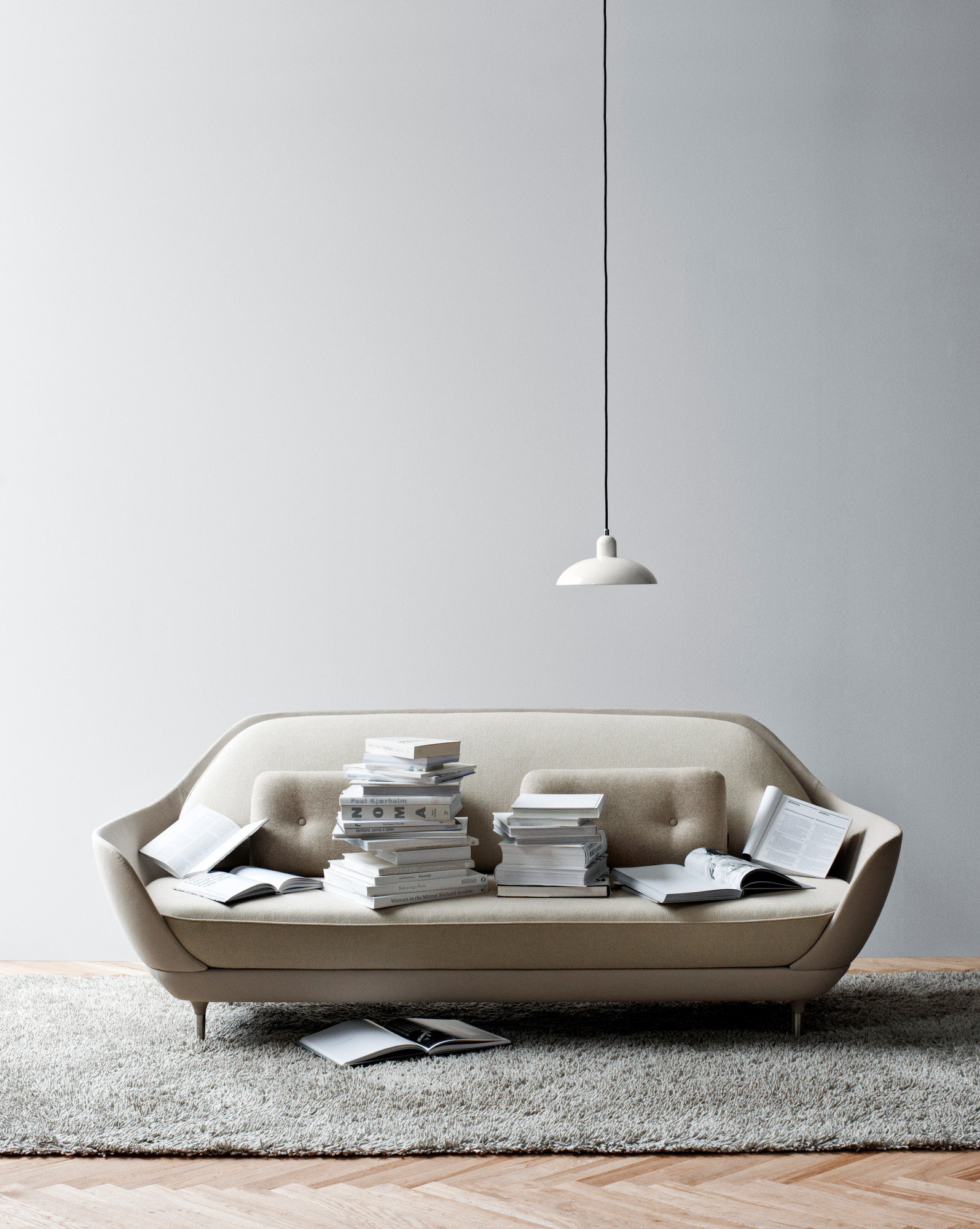 Weiße 6631 P KAISER idell Pendelleuchte von Fritz Hansen über Sofa mit Büchern.