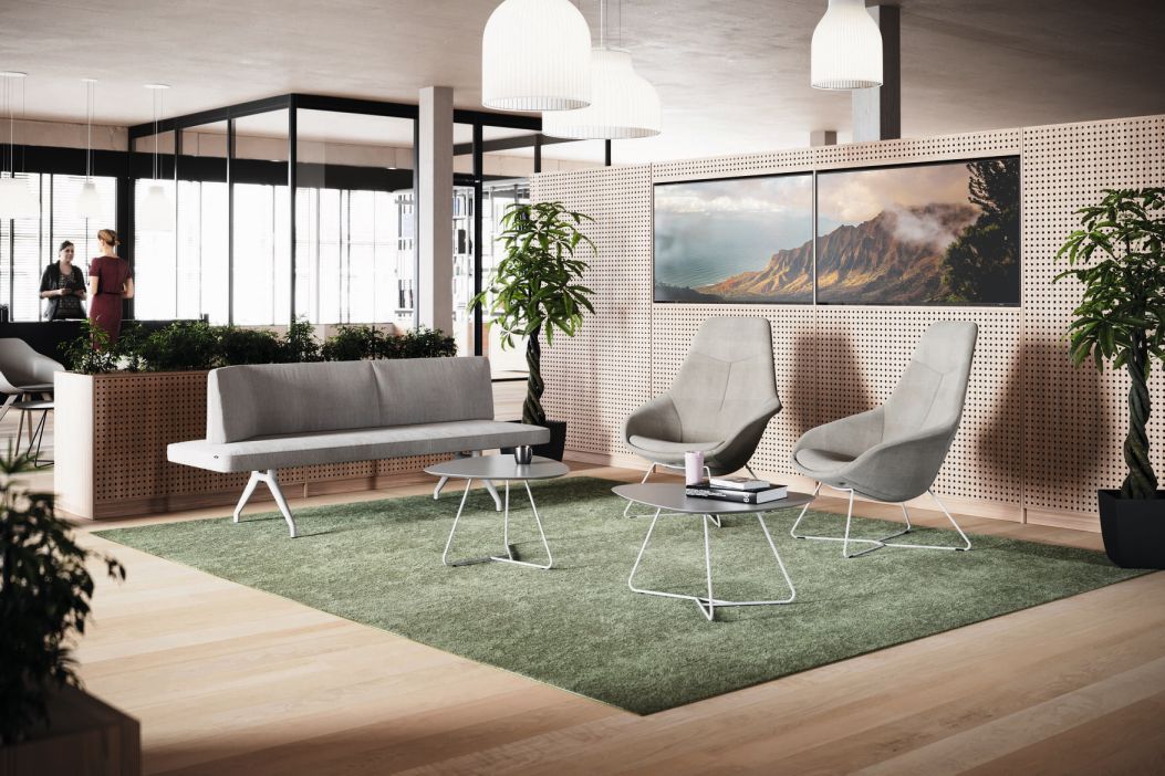 Heller Empfangsbereich mit grauem Yonda Loungesessel von Wilkhahn, Sofa und Couchtischen auf grünem Teppich.