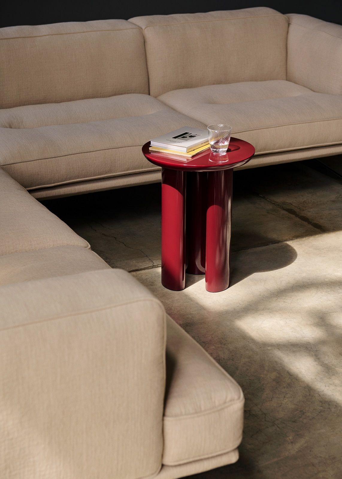 Beiges Inland AV41 Sofa von AndTradition mit rotem Beistelltisch, Buch und Glas Wasser im modernen Wohnzimmer.