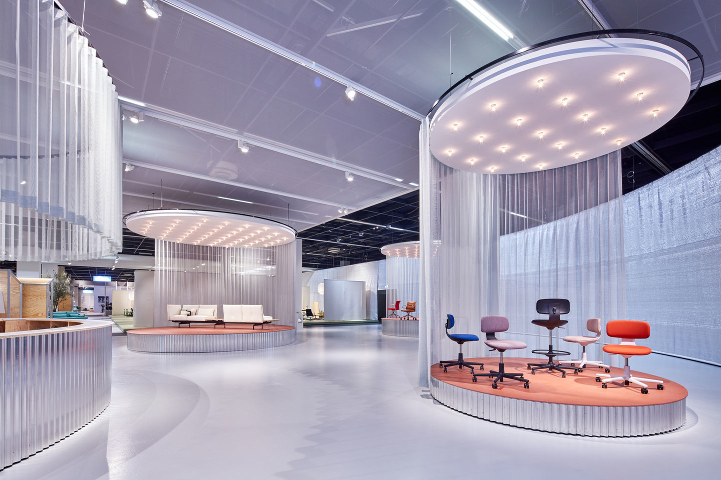 Ausstellung mit verschiedenen farbigen Rookie Bürodrehstühlen von Vitra auf einer erhöhten Plattform.