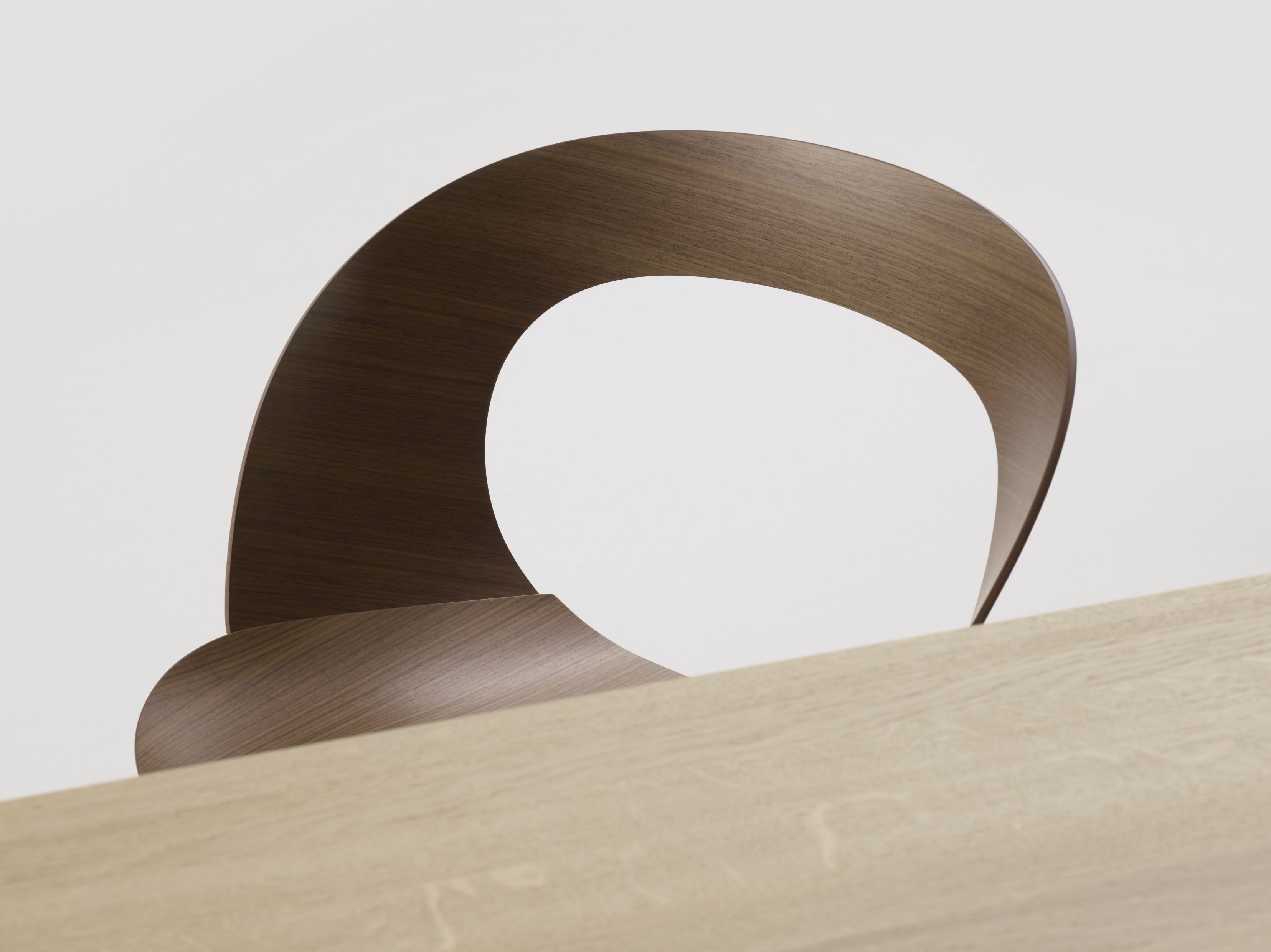 Detailaufnahme des Brunner Mudra Stuhls mit geschwungener Rückenlehne aus Holz auf einem Holztisch.
