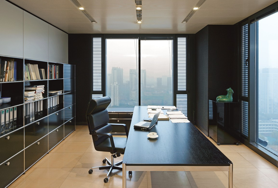 Modernes Büro mit USM Haller Tisch, schwarzem Bürostuhl, Regalsystem und Blick auf die Skyline.