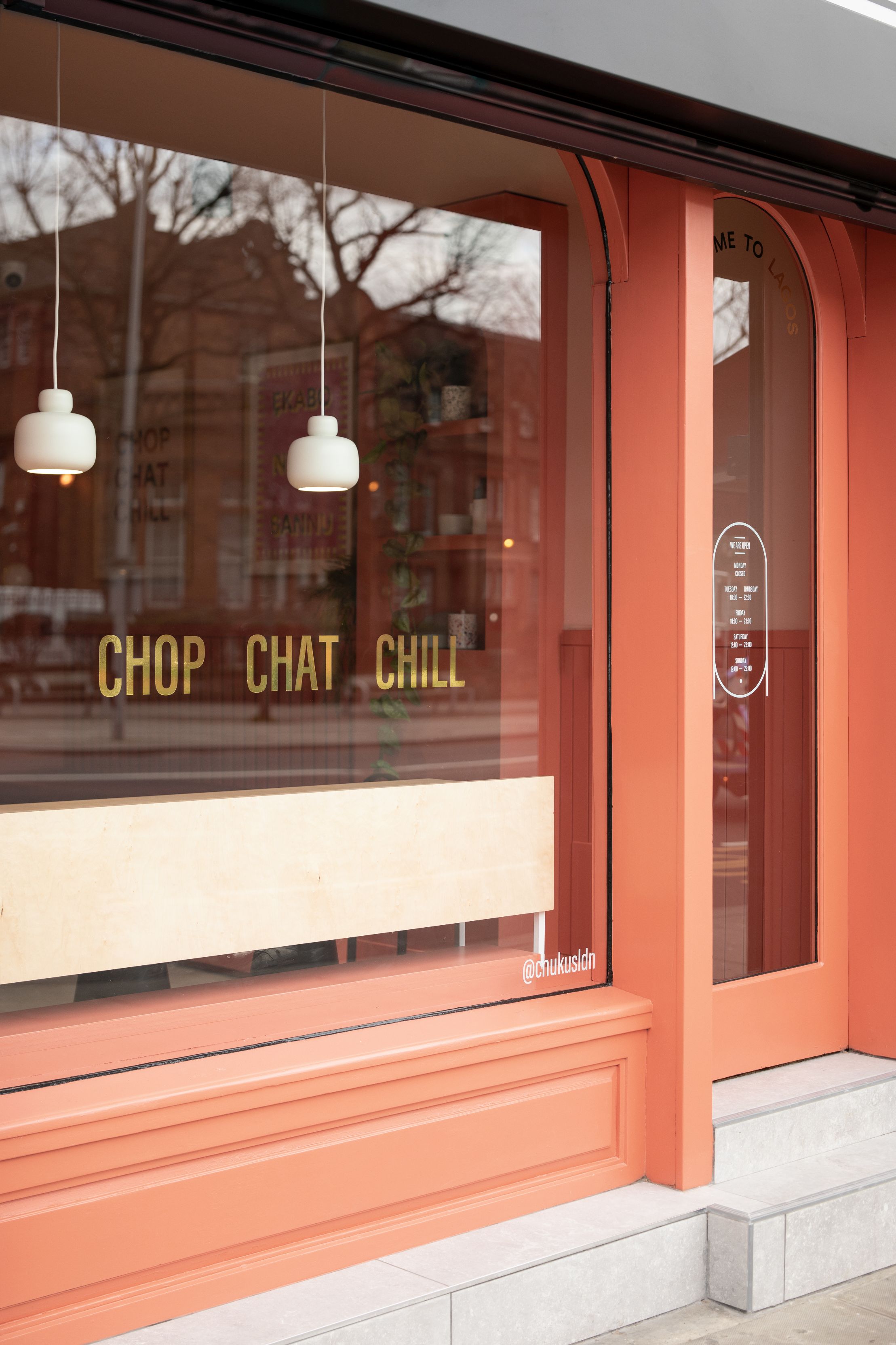 Zwei kleine, weiße Stone Pendant Pendelleuchten von Woud hängen vor einem Schaufenster mit goldener Schrift.