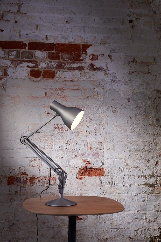 Anglepoise Type 75 Tischleuchte in Alpinweiß auf Holztisch vor einer Backsteinwand.
