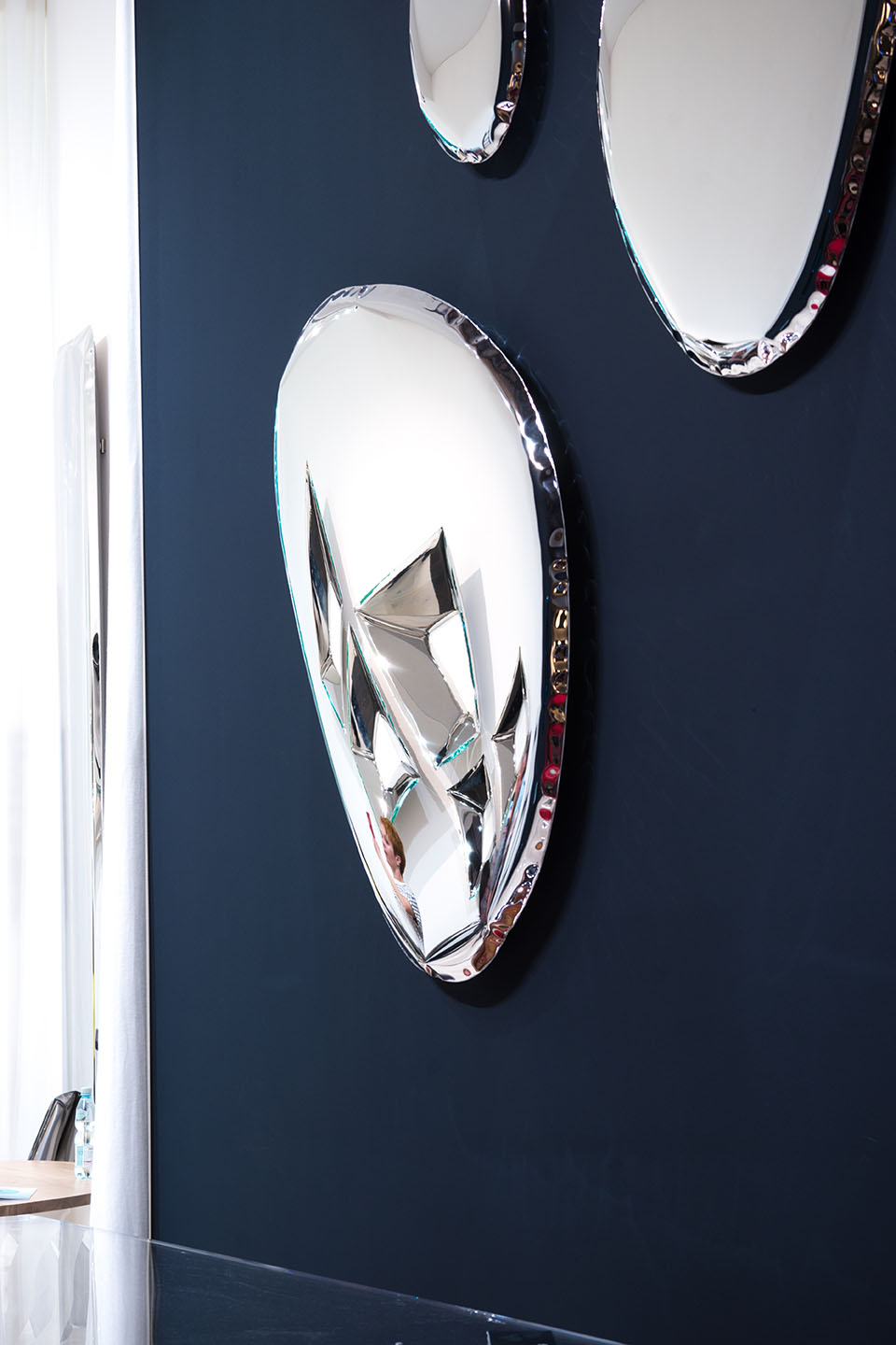 Tafla Spiegel von Zieta, ein moderner Design Wandspiegel mit polierter Oberfläche an einer blauen Wand.
