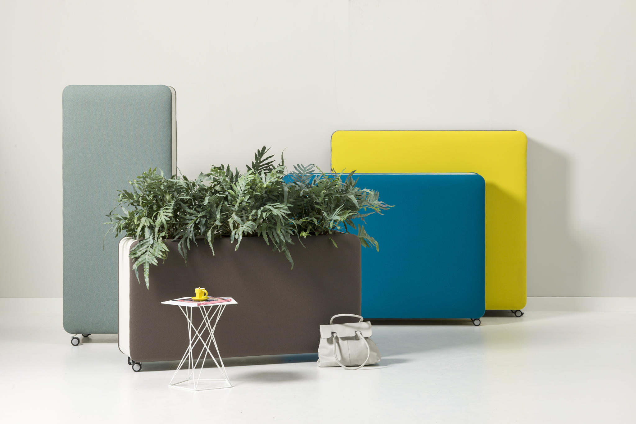 Cascando Pillow Space Akustik-Raumteiler in verschiedenen Farben mit Pflanzen, kleinem Tisch und Handtasche im Büro.