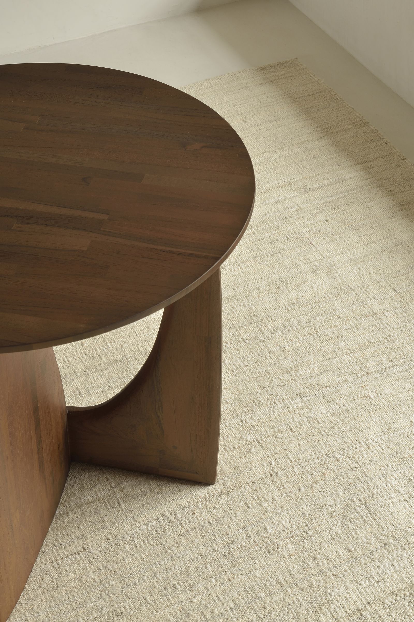 Detailaufnahme: Sandfarbener Ethnicraft Kilim Teppich neben einem runden Holztisch. Hochwertiger, gewebter Teppich.