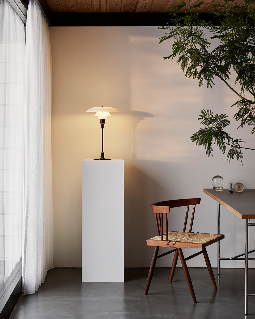 Elegante Tischleuchte mit dreischirmigem Design auf weißem Sockel, stilvolle Innenraumgestaltung mit Holzstuhl und Pflanzen.