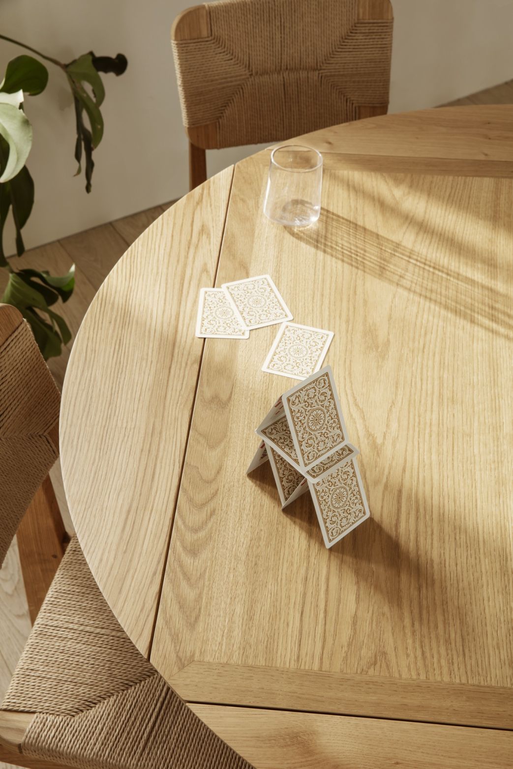 Detailaufnahme des Gubi B-Table Esstischs aus Eiche mit Spielkarten und Stuhl im Hintergrund.