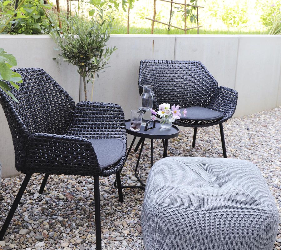 Cane-Line Vibe Sessel mit Kissen in Hellgrau und passendem Pouf im Garten.