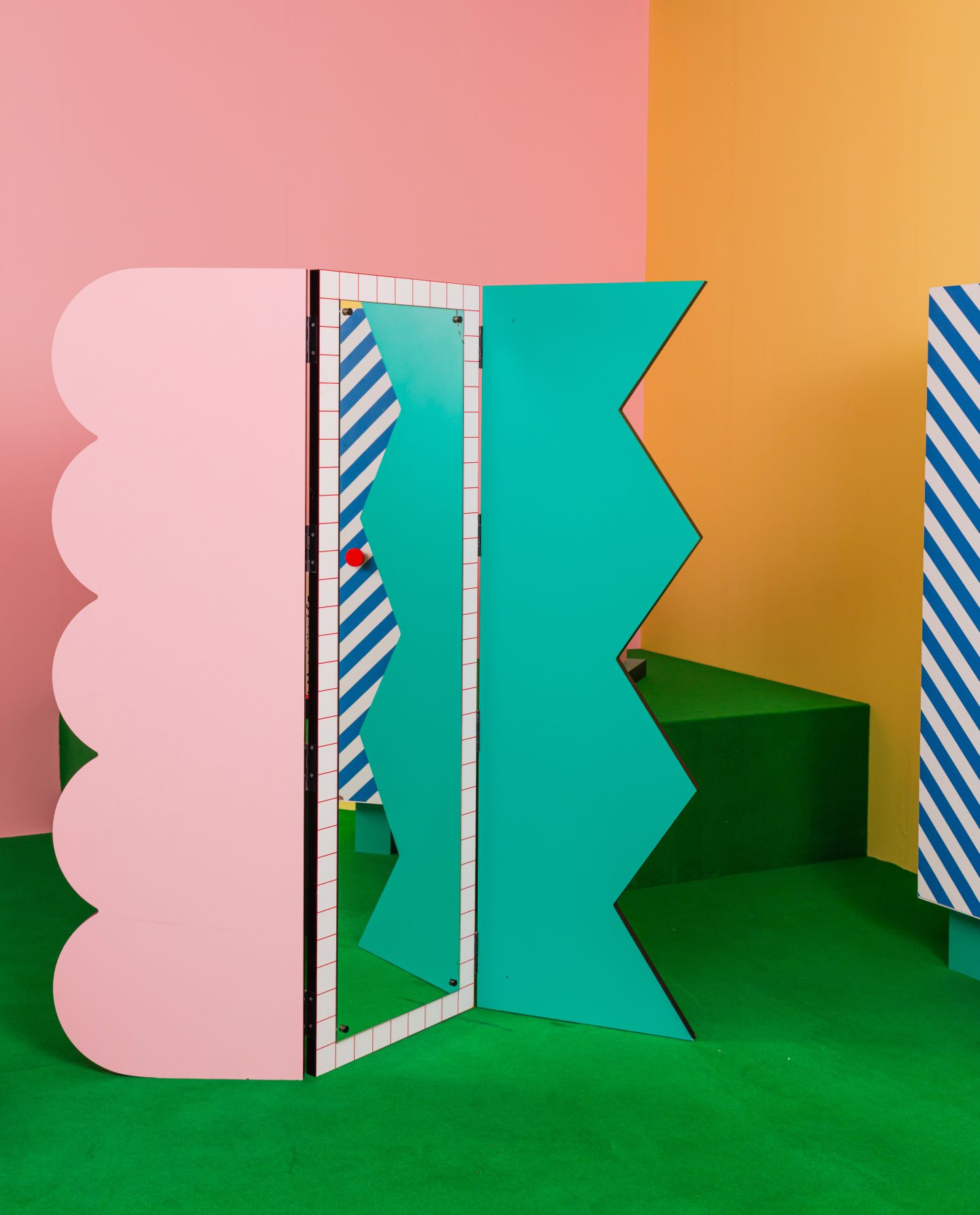 Farbenfroher Seletti Superscreen Raumteiler mit rosa Wolkenform, türkisfarbenen Zickzacklinien und blau-weiß gestreiften Elementen auf grünem Teppich.