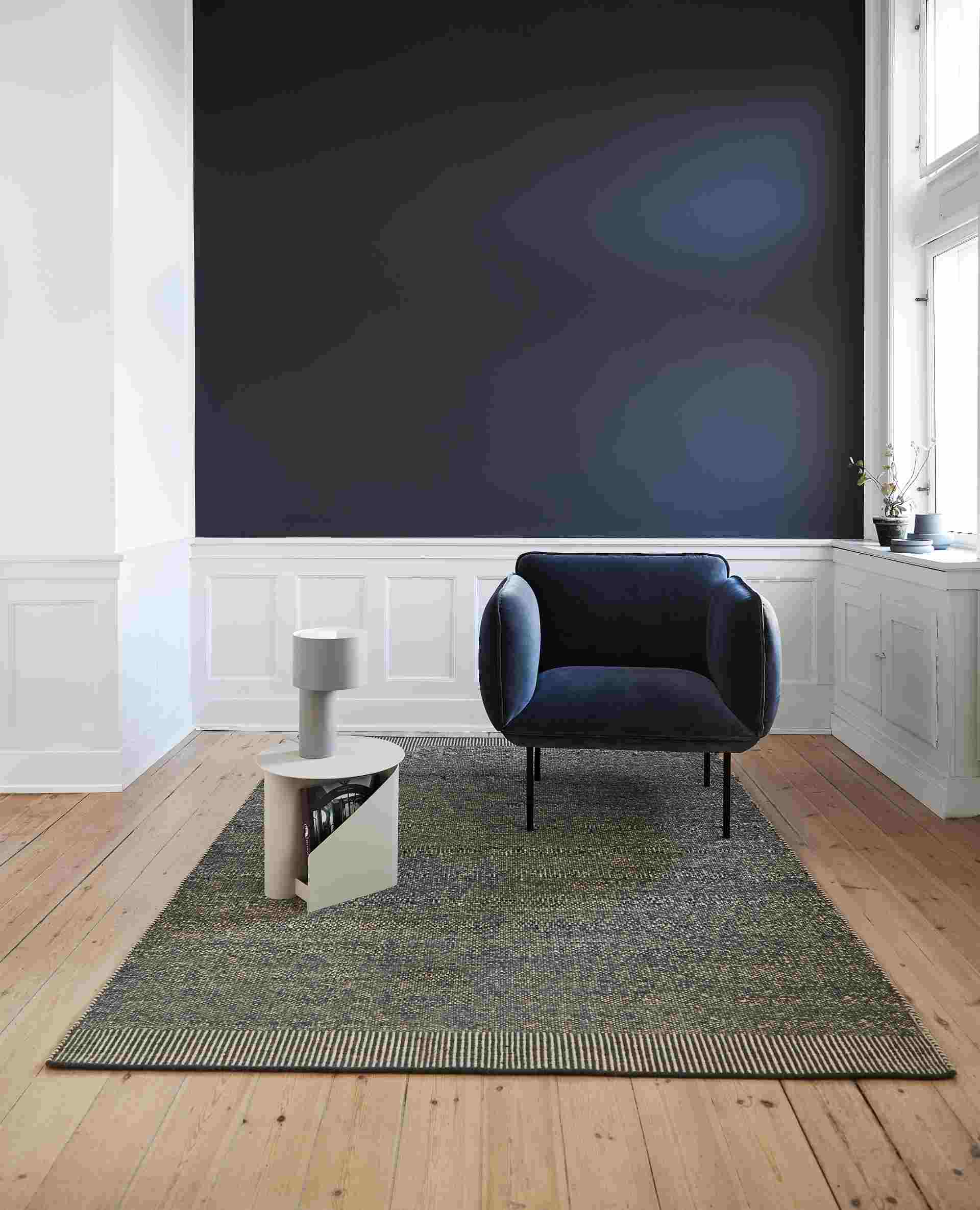 Rombo Rug Teppich in Mossgrün und Weiß im Wohnzimmer mit Sessel und Beistelltisch.
