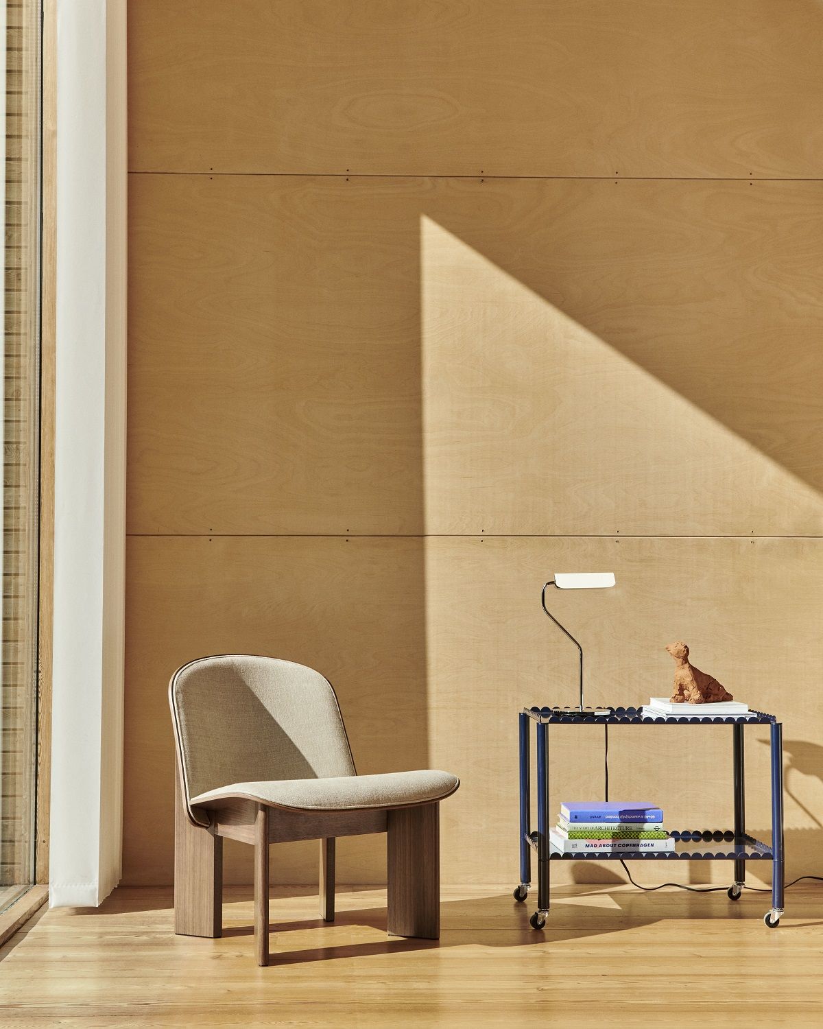 Beiger Chisel Lounge Chair Sessel von Hay mit Vollpolsterung und Holzgestell neben blauem Beistelltisch.