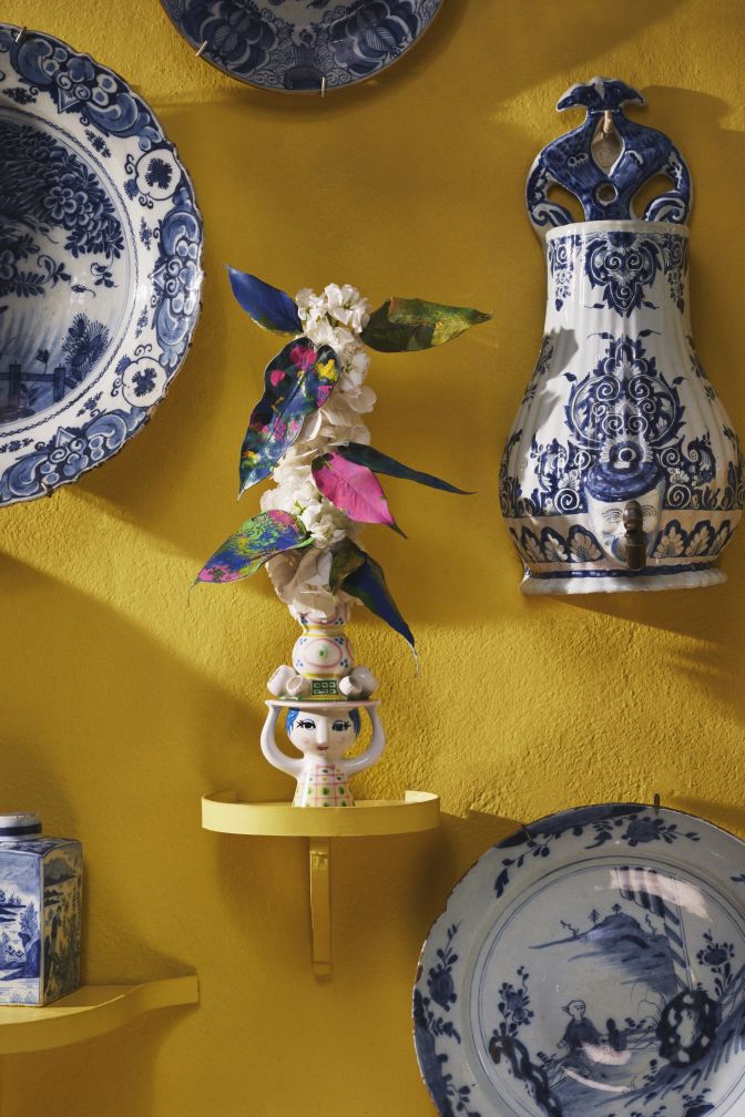 Detailaufnahme des Bjorn Wiinblad Lady with Hat Kerzenständers, dekorative Keramikfigur mit Blumen auf gelber Wand.