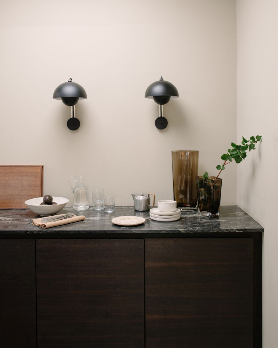 Zwei Flowerpot VP8 Wandleuchten von AndTradition in Schwarz über einem dunklen Holzschrank mit Dekoration.
