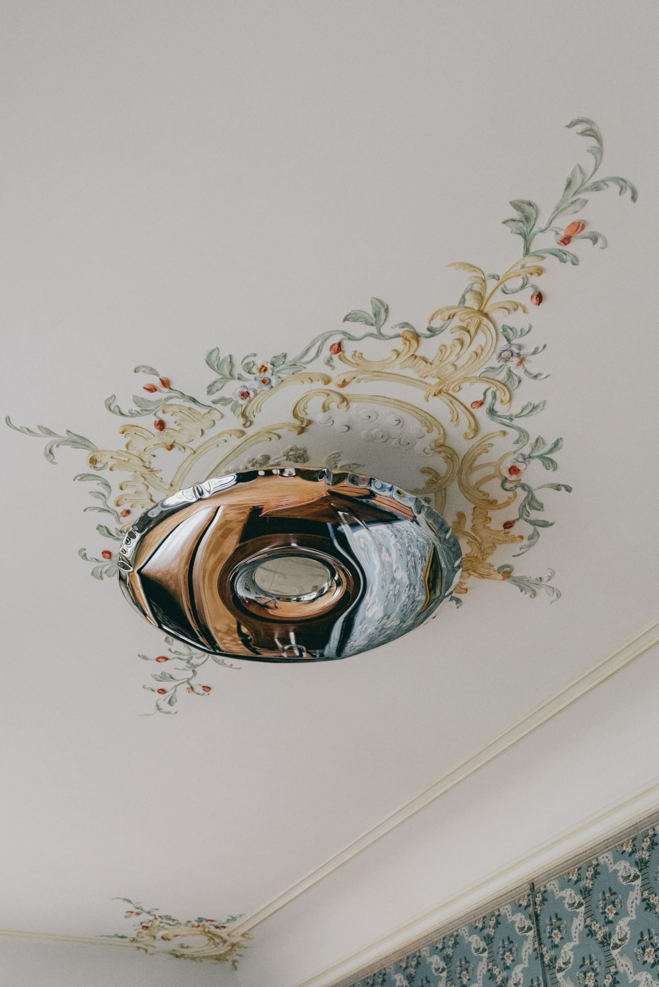 Moderne Deckenleuchte aus Chrom, montiert an einer verzierten Decke mit floralen Malereien. Design Lampe für Wohnzimmer.