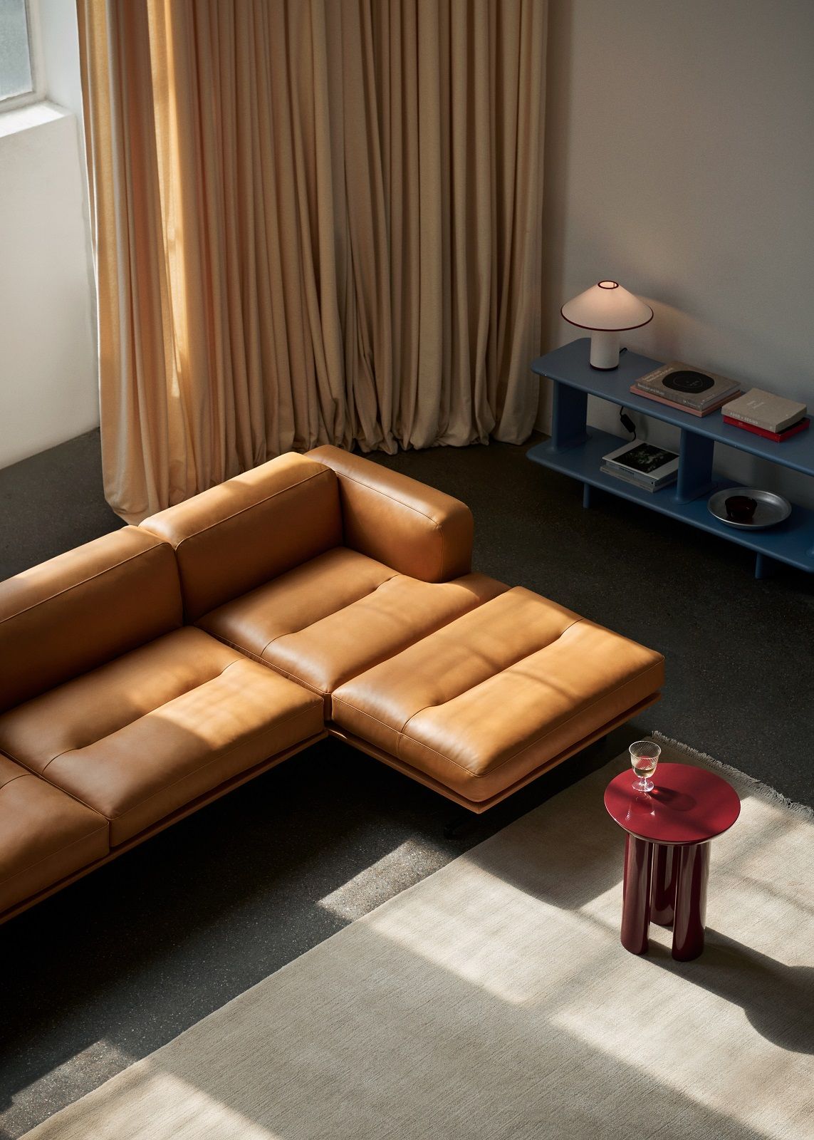 AndTradition Inland AV41 Ledersofa in hellem Braun, kombiniert mit rotem Beistelltisch und blauem Regal.