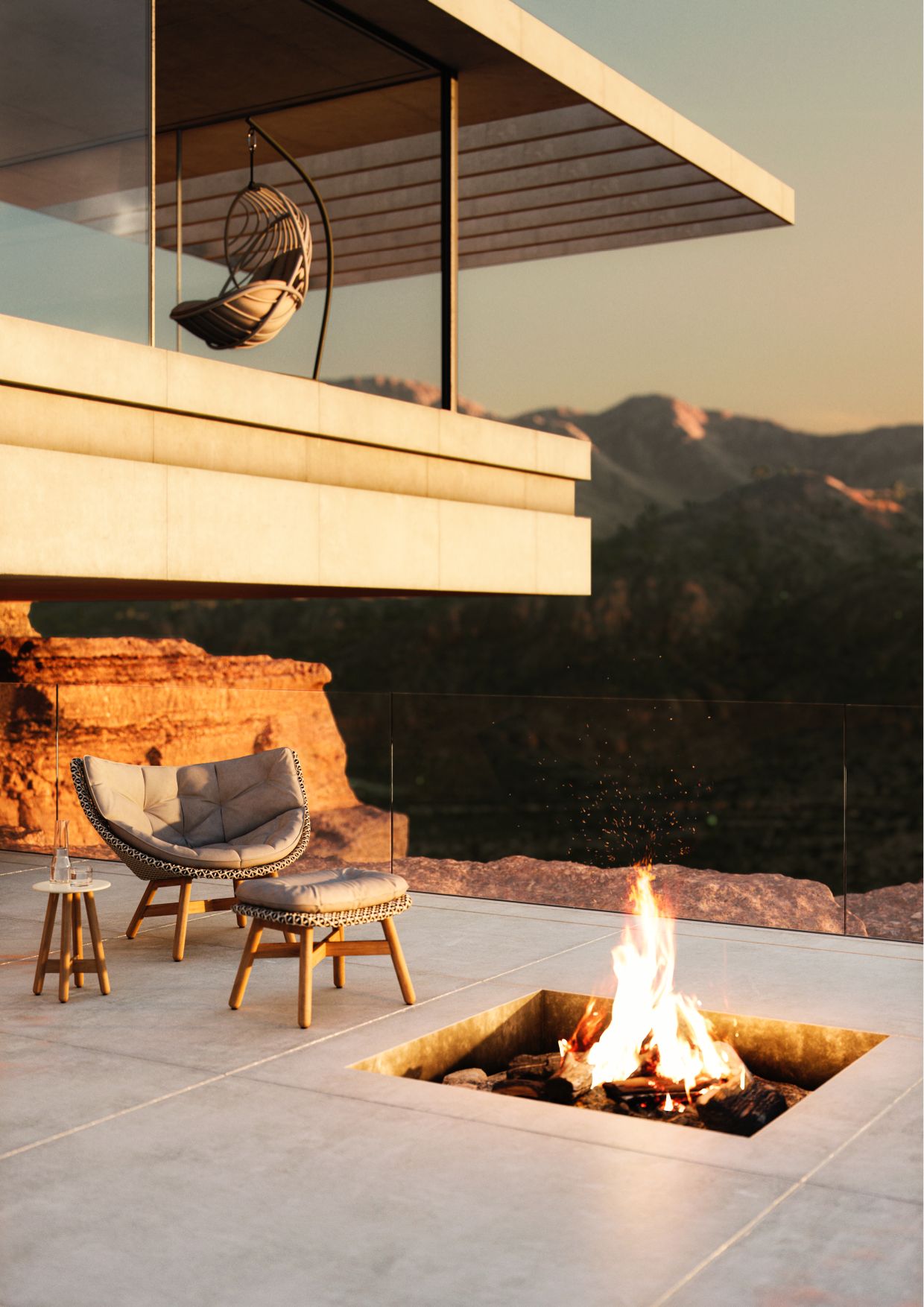 Mbrace Hocker mit Polster von Dedon neben Feuerstelle auf Terrasse mit Bergblick.