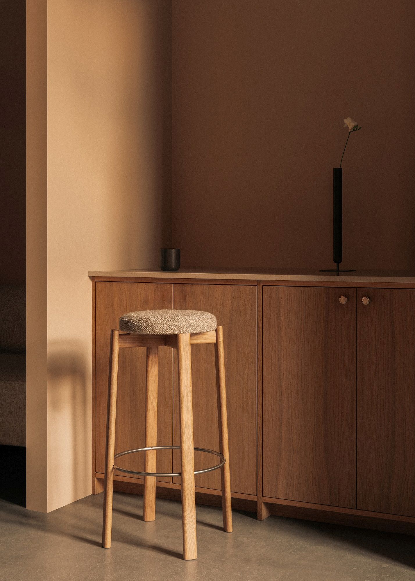 Passage Bar Stool Barhocker von Audo Copenhagen aus Holz mit Stoffbezug vor Holzschrank.
