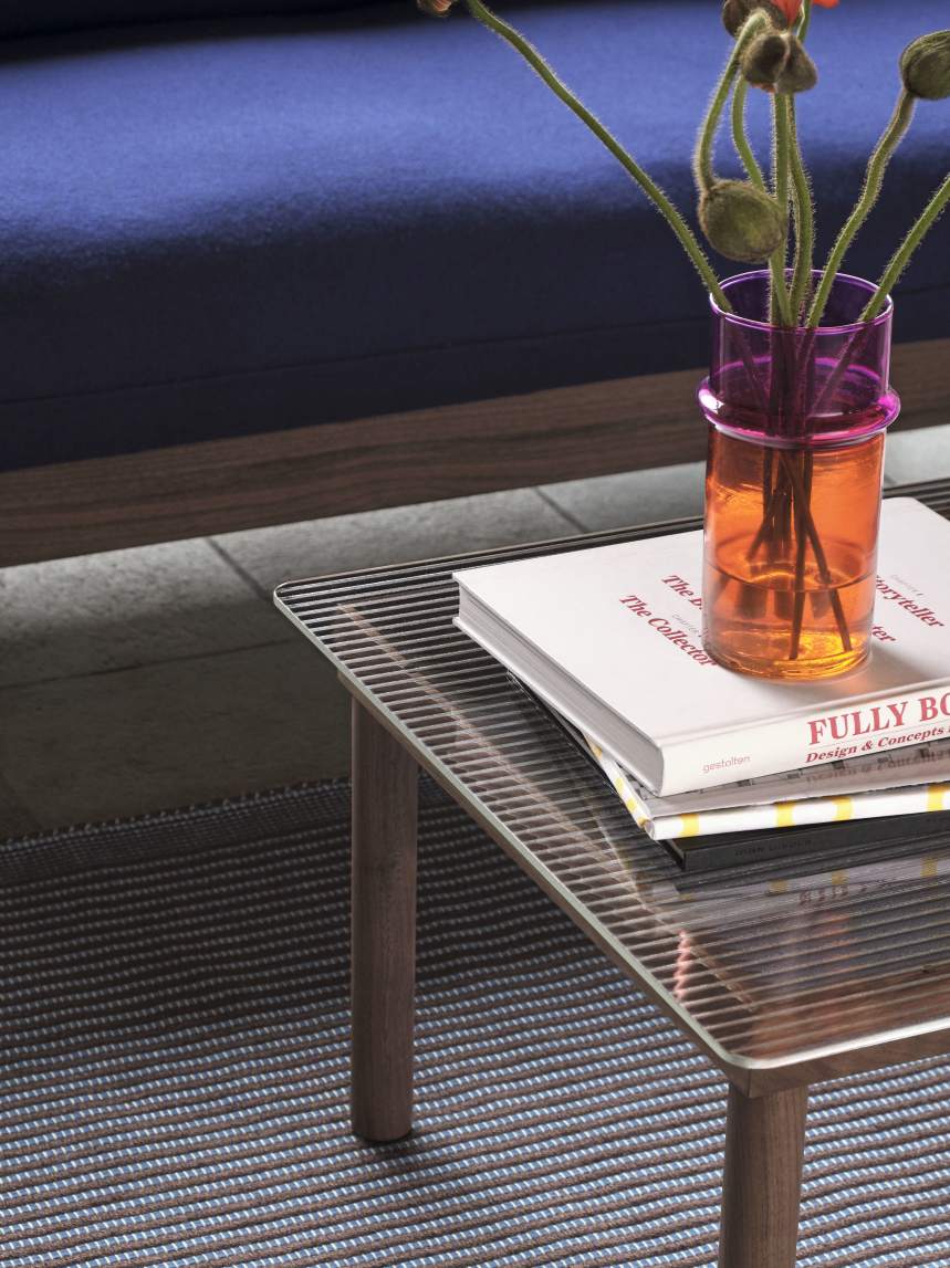 Detailaufnahme des Hay Kofi Couchtisches mit Glasplatte, Büchern und einer Vase mit Blumen.