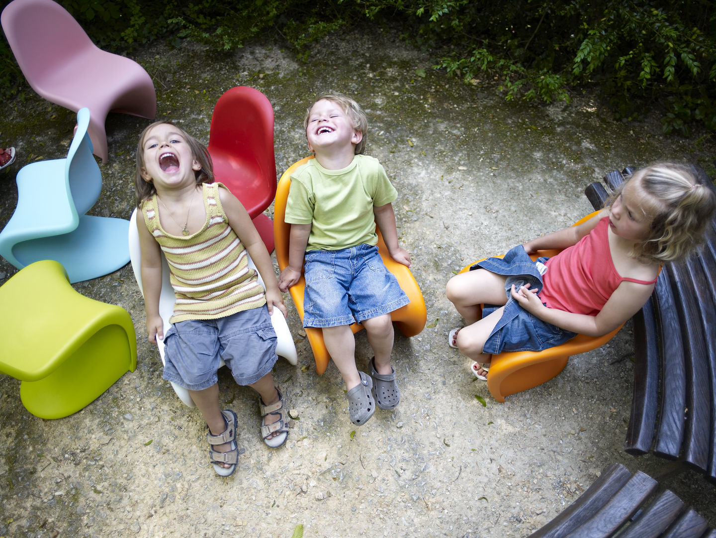 Kinder sitzen auf bunten Panton Junior Stühlen von Vitra im Freien. Design Kinderstuhl.