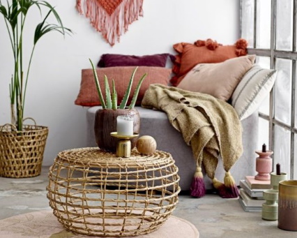 Runder Couchtisch aus Rattan im Boho-Stil mit Dekoration und Kissen für ein gemütliches Wohnzimmer.