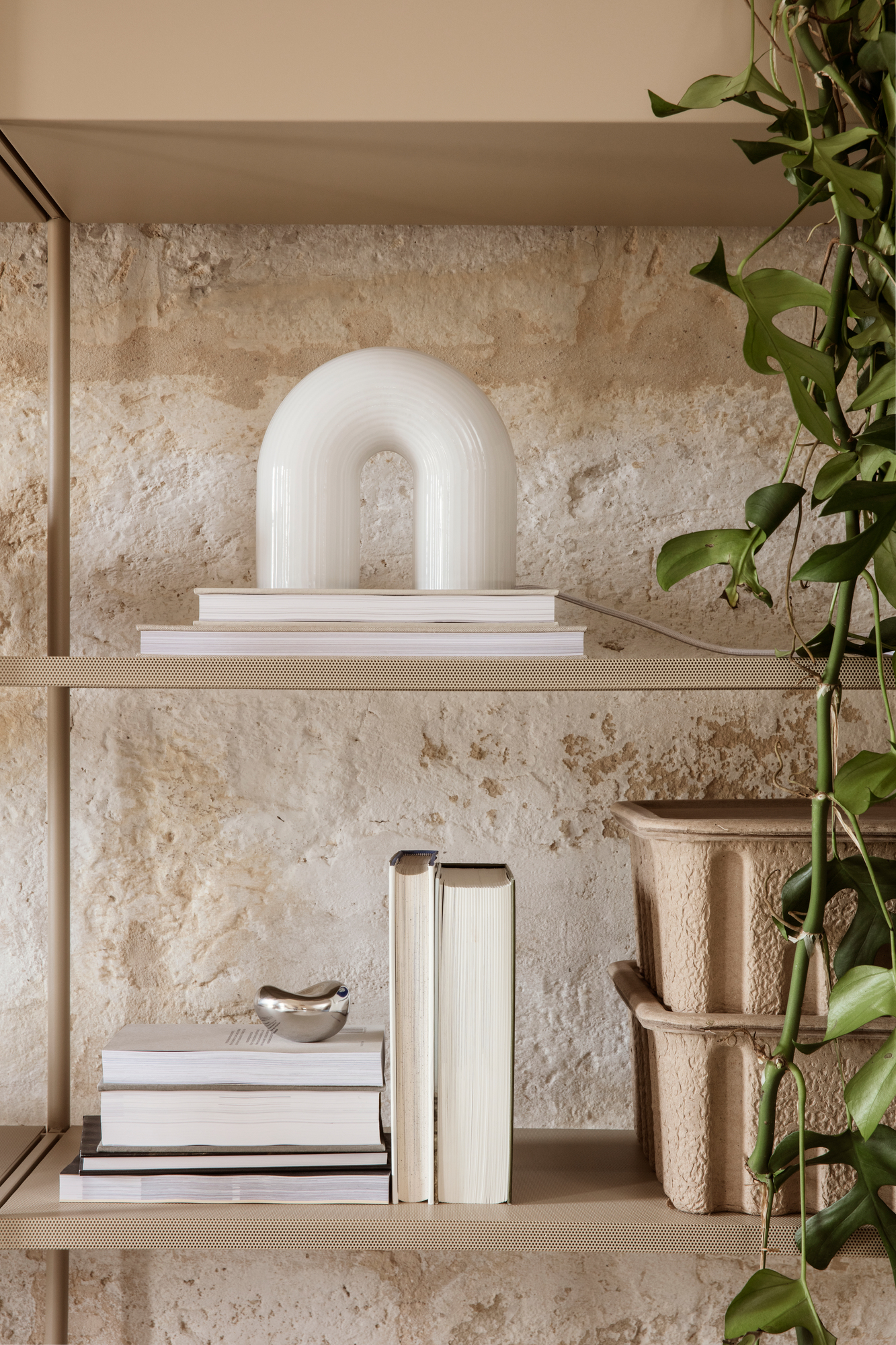Nahaufnahme der Ferm Living Vuelta Tischleuchte, eine moderne Bogenlampe aus Opalglas, auf einem Bücherregal.