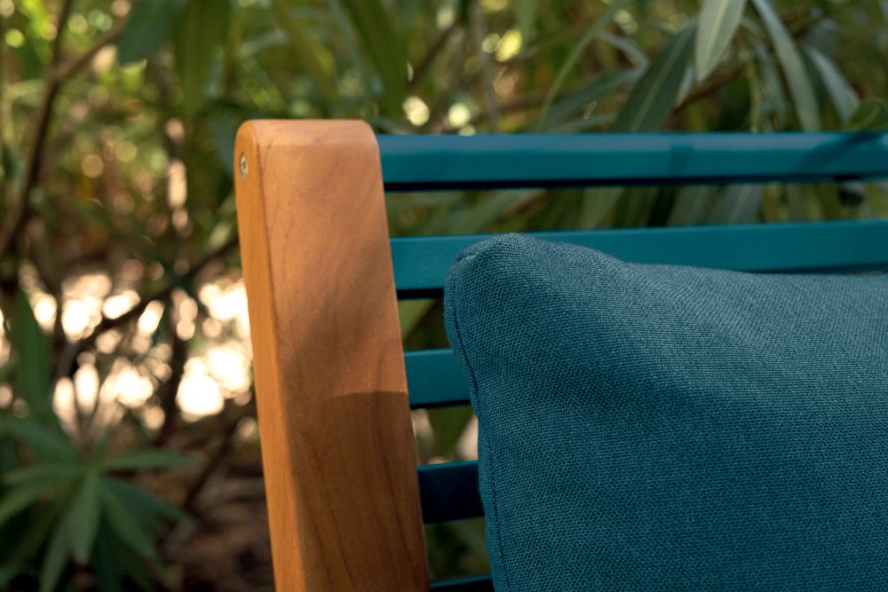 Detailaufnahme: Somerset Sessel von Fermob, Outdoor-Möbel mit blauem Kissen und Holzarmlehne.