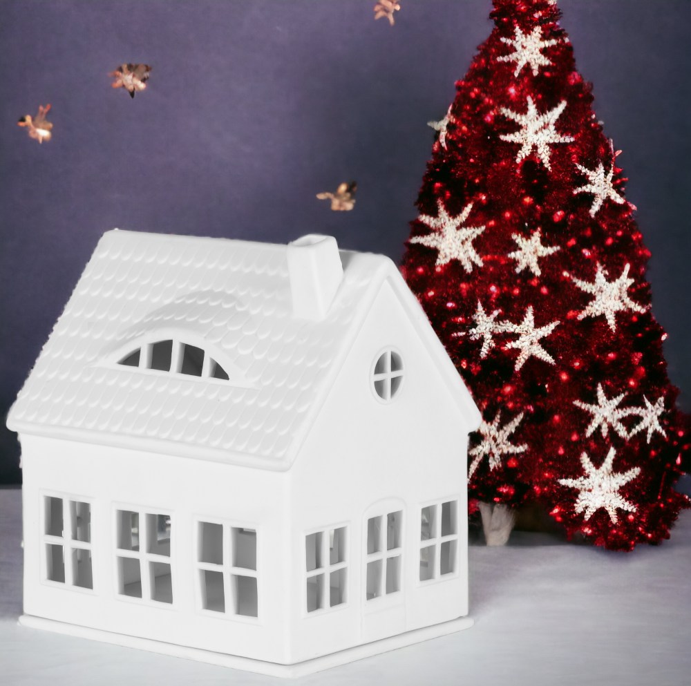 Weißes Räder Lichthaus Gaubenhaus aus Porzellan mit Fenstern und Schornstein, neben rotem Weihnachtsbaum mit Sternen.